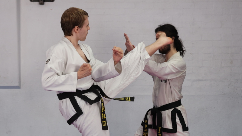 Daniel Beard performing a twisting kick towards a fellow black belt.